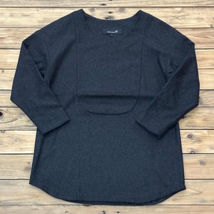 May include: Dark gray long-sleeve shirt with a scoop neck and a unique front panel design. The shirt has a curved hemline and a small tag near the neckline. The fabric appears to be a soft, medium-weight material.