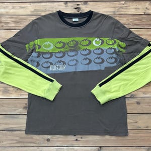 Op de afbeelding: Een shirt met lange mouwen met een grijze body en neon groene mouwen. Het shirt heeft een horizontaal ontwerp met groene en blauwe vormen en het woord "KILLERLOOP" in het wit.