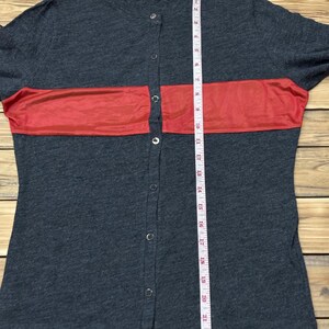 Puede incluir: Una camisa gris oscuro con botones y una franja roja horizontal en el pecho. La camisa tiene mangas cortas y una cinta m&eacute;trica se coloca verticalmente en la parte delantera. La camisa tiene la palabra "wish" impresa en la parte superior.