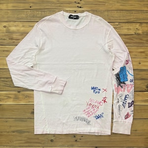 May include: White long-sleeve shirt with graffiti-style text and graphics in blue, pink, and black. The shirt features the text "WHAT THE FUCK", "MILANO", and "DSQUARED2". The right sleeve is covered in various drawings and text.
