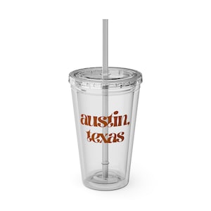 May include: A clear plastic tumbler with a lid and straw. The tumbler features the words "austin, texas" in a brown, retro font. The tumbler is designed for cold beverages.