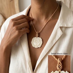 May include: A necklace featuring a round, off-white carved pendant with a floral rose design, suspended from a braided tan cord. The pendant is attached to the cord with a decorative macrame knot. The text Detail Macro View is visible.