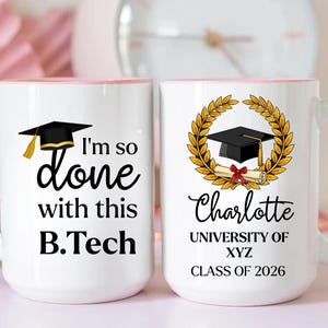 May include: Two white ceramic mugs with pink handles and rims. One mug has the text "I'm so done with this B.Tech" and a graduation cap graphic. The other mug features a graduation cap, laurel wreath, and the name "Charlotte", university details, and "Class of 2026".