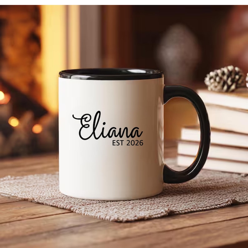 May include: A white ceramic mug with a black handle and the text "But First, Coffee" in a bold, black font. The mug is sitting on a wooden surface. The mug is 4 inches tall.