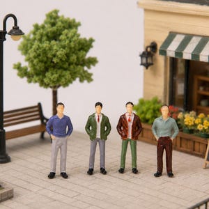Può includere: Figurine in miniatura di quattro persone in abbigliamento casual in piedi su un'area pavimentata con mattoni. Una panchina, un lampione e un edificio con una tenda a strisce sono sullo sfondo. La scena è un diorama.