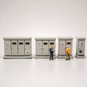 Puede incluir: Miniaturas de subestaciones eléctricas grises con dos pequeños trabajadores con ropa de construcción. Las subestaciones tienen puertas, ventanas y señales de advertencia. Los trabajadores llevan cascos y chalecos de seguridad.