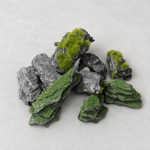 May include: A collection of dark grey, textured rock-like pieces featuring patches of bright green artificial moss. The stones have jagged, layered surfaces and irregular shapes, with some pieces covered in dense green flocking and others bare.