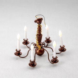 May include: Miniature chandelier with six white candle lights. The chandelier has a bronze finish with a gold chain and wiring. The candle lights are evenly spaced around the fixture.