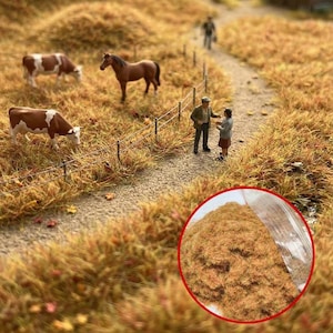 Könnte beinhalten: Miniatur-Diorama-Szene mit einem Weg, einem Zaun und Figuren von Menschen, Kühen und einem Pferd in einem Feld mit hohem, trockenem Gras. Eine Nahaufnahme zeigt einen Haufen braunes, getrocknetes Gras.