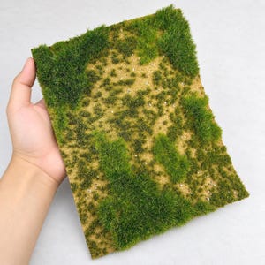 Puede incluir: Una base de diorama rectangular con una superficie de suelo color canela texturizada, cubierta con parches de hierba estática verde vibrante y pequeñas piedras blancas dispersas, diseñada para modelismo y terrenos de juegos de mesa.