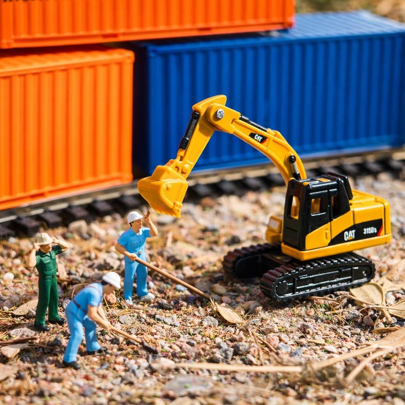 May include: A miniature construction scene featuring a yellow and black CAT excavator with the text "CAT 315D". Three miniature construction workers are present. Orange and blue shipping containers are in the background.