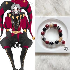 Könnte beinhalten: Ein Armband mit roten, schwarzen und cremefarbenen Perlen. Ein silberfarbener sternförmiger Anhänger und ein Rosenanhänger hängen an dem Armband. Das Armband liegt auf einem weißen Teller.