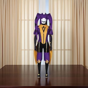 May include: A purple and gold jester costume with a smiling face mask. The costume features a diamond pattern on the sleeves and shorts, with a gold collar and accents. The jester's hat has long, purple and black striped horns.