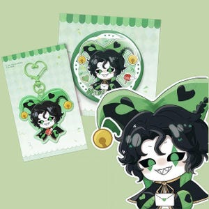 May include: A selection of jester-themed items in green and black. The image shows a keychain, a badge, and a sticker, each with a cartoon jester character wearing a heart-shaped hat and bells. The background is a pale green.