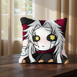 May include: Square decorative pillow featuring an anime-style character with white hair, large yellow eyes, and a sad expression. The pillow has a black and red border and is placed on a wooden surface.