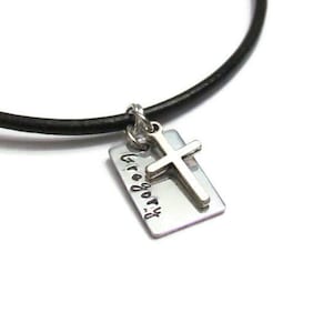 May include: A black leather cord necklace with a silver charm. The charm has the name "Gregory" engraved on it and a small silver cross.