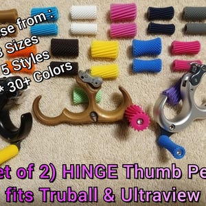 May include: A collection of HINGE thumb pegs in various colors and styles, with the text "Choose from: 3 Sizes, 5 Styles, 30+ Colors" and "(Set of 2) HINGE Thumb Pegs fits Truball & Ultraview". The pegs are designed for archery equipment.