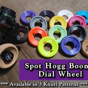 Puede incluir: Una colección de ruedas de ajuste circulares Spot Hogg Boonie en varios colores, incluyendo amarillo, naranja, verde, azul, morado, blanco, negro y beige. Una rueda está unida a un mecanismo de mira de arco. Texto: Spot Hogg Boonie Dial Wheel. Available in 3 Knurl Patterns.