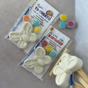 May include: Two DIY plaster butterfly painting kits. Each kit includes a white butterfly figure, paint pots in various colors, and a paintbrush. One kit has the text "Time TO CREATE!" and the other says "It's my BIRTHDAY".