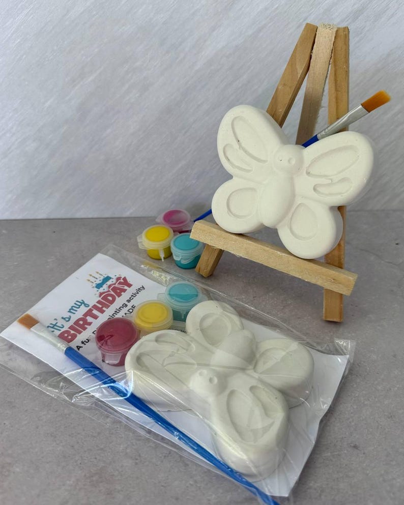 May include: A butterfly-shaped ceramic figurine on a miniature wooden easel, with a paintbrush and small paint pots. A second butterfly figurine is in a clear plastic bag, along with a paint set and a card that reads "It's my BIRTHDAY".