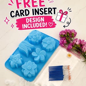 May include: A bright blue silicone mold featuring six distinct floral cavities, accompanied by a clear plastic bag containing a set of small blue-handled paintbrushes, a strip of empty white paint pots, and a text graphic reading FREE CARD INSERT DESIGN INCLUDED!