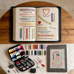 May include: An open book showing embroidery stitch examples with colourful threads. A sewing kit with thread spools, needles, scissors, and other tools sits beside a grey needle case with a stitched house design. A complete embroidery set.