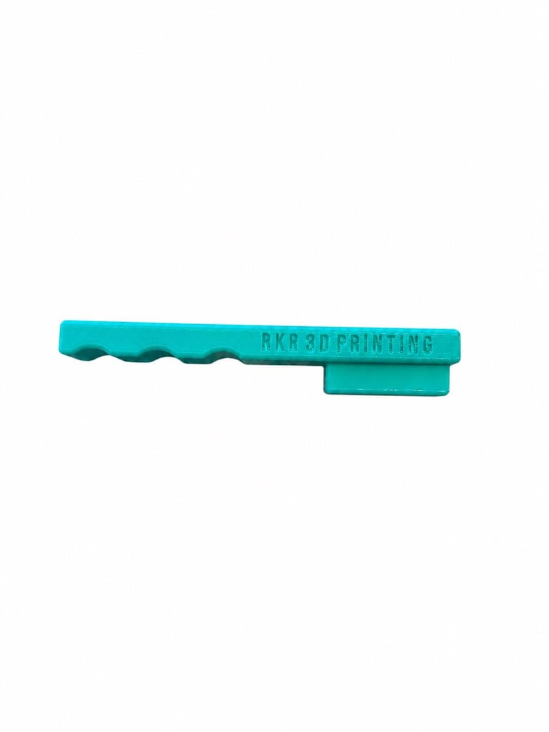 May include: A teal-colored, elongated plastic tool featuring a series of three rounded indentations along one side for grip. The text RKR 3D PRINTING is embossed on the flat surface of the object, which has a rectangular extension on one end.