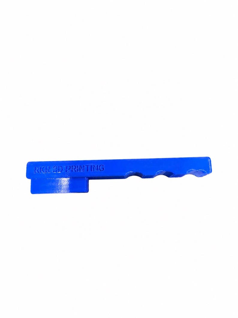 May include: A bright blue, elongated, rigid object with a rectangular base and a handle-like extension featuring three semi-circular cutouts along the top edge. The text RKR 3D PRINTING is embossed on the side of the blue plastic component.