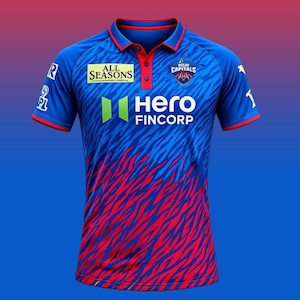 Op de afbeelding: Een blauw en rood poloshirt met een patroon van rode strepen op een blauwe achtergrond. De shirt heeft een rode kraag en bies, met de tekst "ALL SEASONS" en "HERO FINCORP" zichtbaar. De shirt heeft ook de tekst "DELHI CAPITALS".
