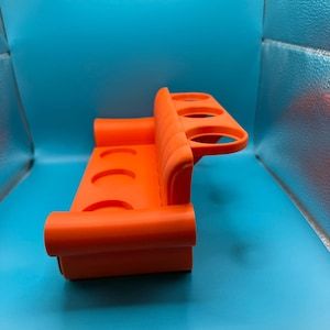May include: Bright orange plastic cup holder with four circular openings. The holder has a curved design with a back and a base, and is designed to hold cups or bottles. The holder is on a blue background.