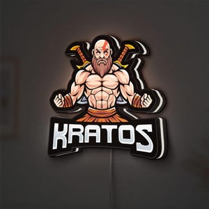 Puede incluir: Un letrero LED con temática de Kratos que presenta un personaje musculoso con una marca roja en la cara y una larga barba, sosteniendo dos espadas. El letrero tiene un fondo negro con detalles en blanco y naranja, y el nombre "KRATOS" se muestra en la parte inferior.