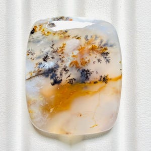 May include: A rectangular dendritic agate gemstone with rounded corners, featuring a translucent white base with intricate black, fern-like branch patterns and warm golden-yellow inclusions throughout the polished stone surface.