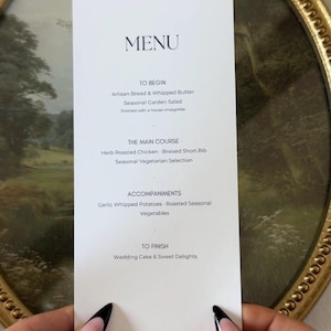 May include: A rectangular white menu card with black text listing courses including Artisan Bread, Herb Roasted Chicken, Braised Short Rib, and Wedding Cake. The menu is printed in a clean, centered font on a smooth, matte paper stock.