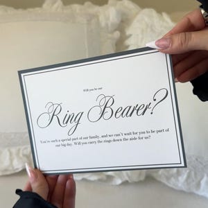 May include: A rectangular white card with a thin black border featuring the text Will you be our Ring Bearer? You're such a special part of our family, and we can't wait for you to be part of our big day. Will you carry the rings down the aisle for us?