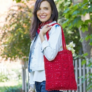 May include: A red crochet tote bag with a square pattern and scalloped edges. The bag has long straps and is filled with white flowers. The bag is carried over the shoulder.