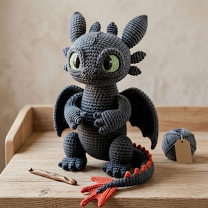 May include: A dark gray crocheted dragon plush toy with large green eyes, small wings, and a long tail featuring bright orange spikes and a fin-like tip. The creature has a textured yarn surface and stands upright on its two feet with small claws.