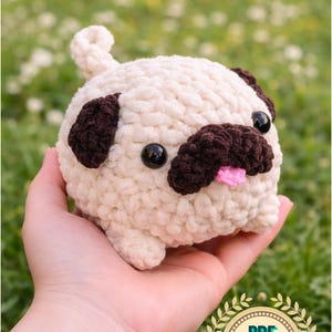 Op de afbeelding: Een gehaakte mopshond met een crèmekleurig lichaam, donkerbruine oren en snuit en zwarte ogen. De mopshond heeft een roze tong die uitsteekt. De afbeelding bevat de tekst "CROCHET - PATTERN-PDF ENGLISH" en een "PDF PATTERN" afbeelding.