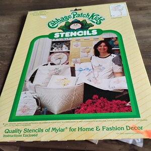 May include: A yellow Cabbage Patch Kids stencil package featuring a green logo and the text Stencils, Quality Stencils of Mylar for Home & Fashion Decor. The packaging displays a photograph of various craft projects including a tote bag.
