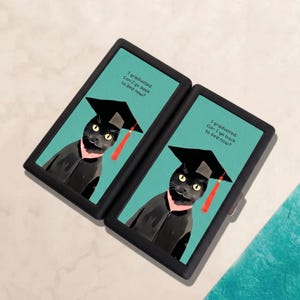 May include: A black rectangular case featuring two identical illustrations of a black cat wearing a graduation cap with a red tassel against a teal background. The text "I graduated. Can I go back to bed now?" is printed above the cat.