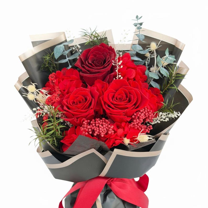 Puede incluir: Un ramo de rosas rojas y otras flores rojas envuelto en papel negro con un borde dorado. El ramo est&aacute; atado con una cinta roja. El arreglo incluye eucalipto y otras plantas verdes.