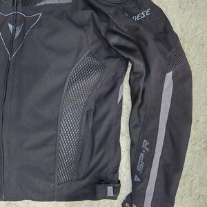 Peut inclure: Veste de moto noire avec des d&eacute;tails gris et des panneaux en mesh. Comprend le logo de la marque sur la poitrine et la manche. La veste a une fermeture &eacute;clair et une coupe ajust&eacute;e, pour la moto.