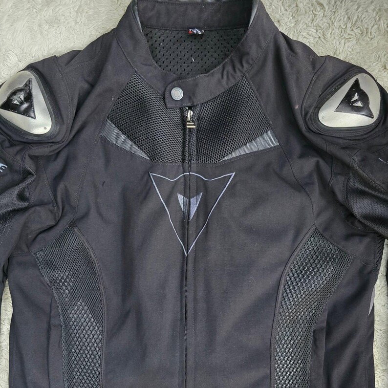 Peut inclure: Veste de moto noire avec des panneaux en mesh et des d&eacute;tails argent&eacute;s. Elle est dot&eacute;e d'une fermeture &eacute;clair frontale, d'un col montant et de protections aux &eacute;paules. La veste porte un logo sur la poitrine et les &eacute;paules.