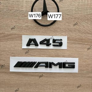 Op de afbeelding: Een set zwarte auto-emblemen inclusief een rond logo met een driepuntige ster met de tekst W176 en W177, een A45-badge en een AMG-embleem. De emblemen zijn matzwart en gepresenteerd op witte achtergrondstrips voor toepassing op een voertuig.
