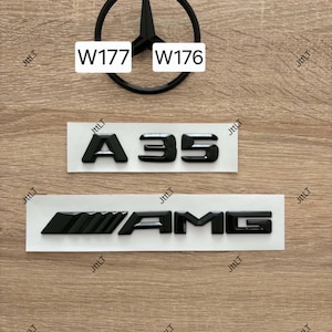 Könnte beinhalten: Ein schwarzes Mercedes-Benz Stern-Emblem, ein schwarzes A35-Emblem und ein schwarzes AMG-Emblem. Das Stern-Emblem ist über den Schriftzügen angeordnet. Der Text W177 und W176 ist auf weißen rechteckigen Etiketten über dem Stern abgedruckt.
