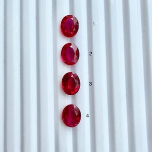 May include: Four oval-cut, vibrant red gemstones arranged in a vertical column. Each gemstone is faceted and displays a deep crimson hue. The stones are numbered 1 through 4 in black text to the right of each corresponding gem, set against a white background.