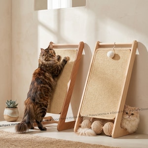 Op de afbeelding: Twee houten krabpalen voor katten met geweven sisal oppervlakken. Eén paal heeft een kat die eraan krabt. De andere paal heeft een hangend speeltje en een kat die eronder rust. De palen zijn lichtbruin en beige.