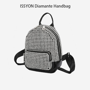 Puede incluir: Una pequeña mochila negra y plateada cubierta de pedrería, con un asa superior y correas ajustables. La bolsa tiene un bolsillo frontal con cremallera y el texto "ISSYON Diamante Handbag" en la parte superior.