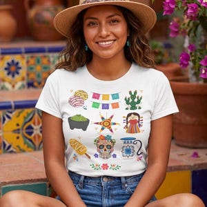 May include: A white short-sleeve t-shirt featuring a colorful graphic print of various icons including conchas, papel picado, a cactus, a molcajete, a star-shaped piñata, a doll, elote, a decorated sugar skull, and a floral pitcher.