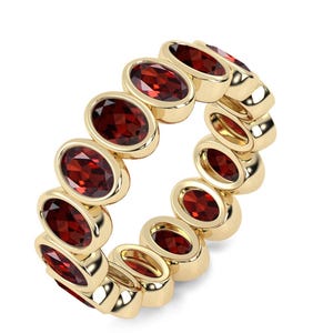 May include: A gold ring featuring a series of oval-cut, deep red gemstones. The gemstones are set in individual gold bezels, creating a continuous band. The ring is displayed against a white background, highlighting the contrast between the gold and the red stones.