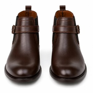 May include: A pair of brown leather Chelsea boots. The boots have a rounded toe, a buckle strap across the ankle, and elastic side panels. The boots are set against a white background.